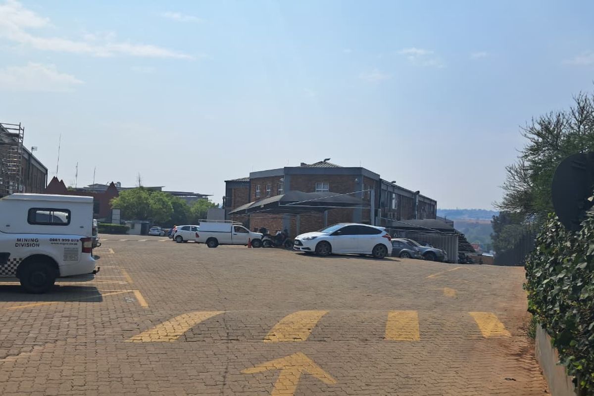 Exterior view of an industrial property featuring a paved parking lot with shade cloth carports and brick building structures.