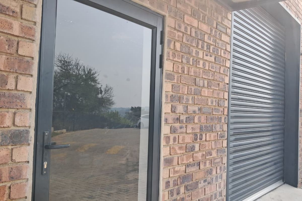 Exterior view of an industrial unit featuring a face brick facade, a secure glass entrance door, and a roller shutter door for vehicle access.