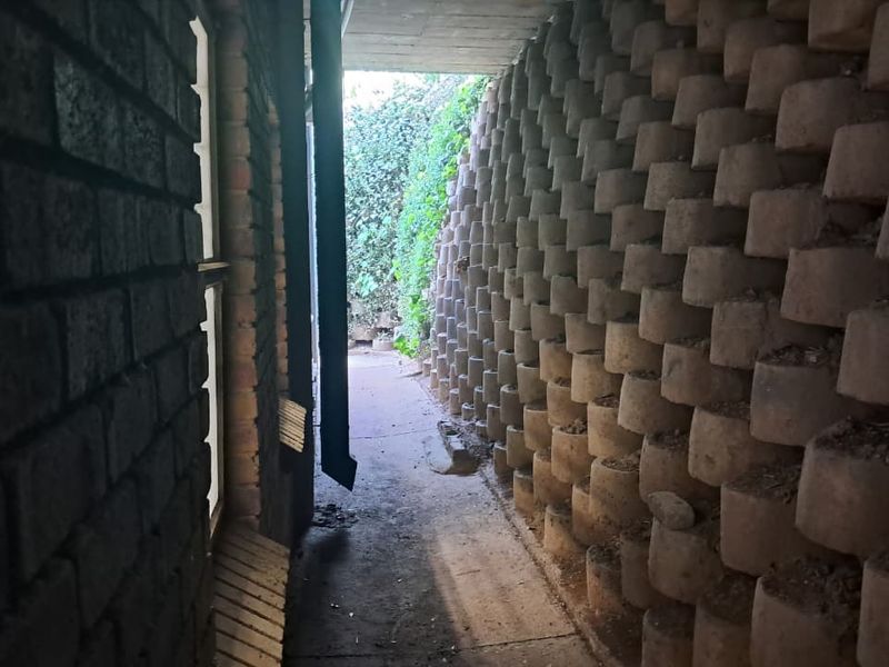 A narrow exterior side passage featuring a concrete retaining wall and paved walkway, providing access along the side of the industrial building.