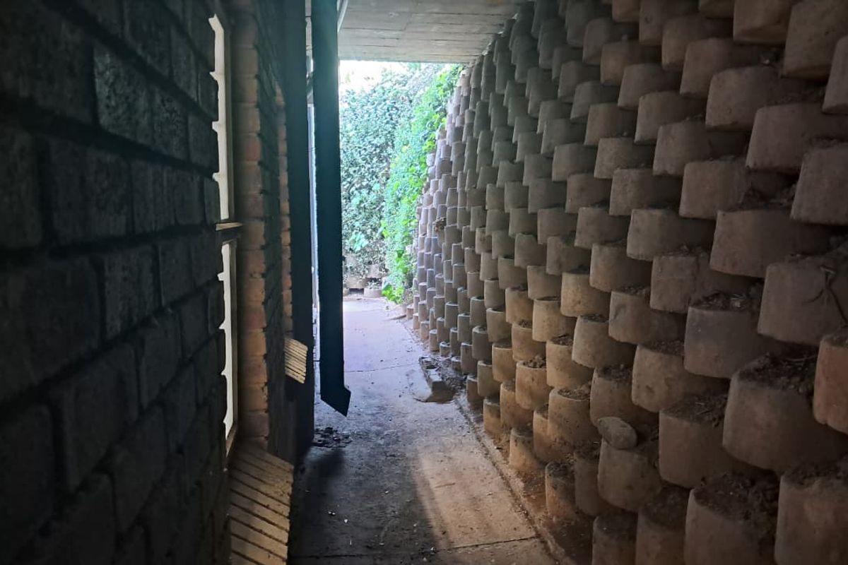 A narrow exterior side passage featuring a concrete retaining wall and paved walkway, providing access along the side of the industrial building.