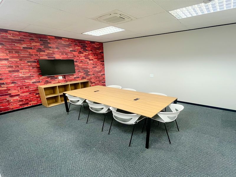 A professional office meeting room featuring a brick-effect accent wall, suspended ceiling with recessed lighting, and durable carpet tile flooring.