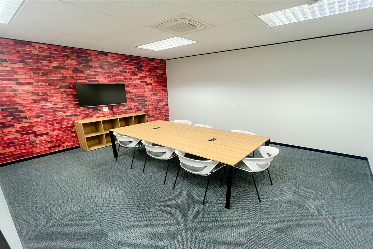 A professional office meeting room featuring a brick-effect accent wall, suspended ceiling with recessed lighting, and durable carpet tile flooring.