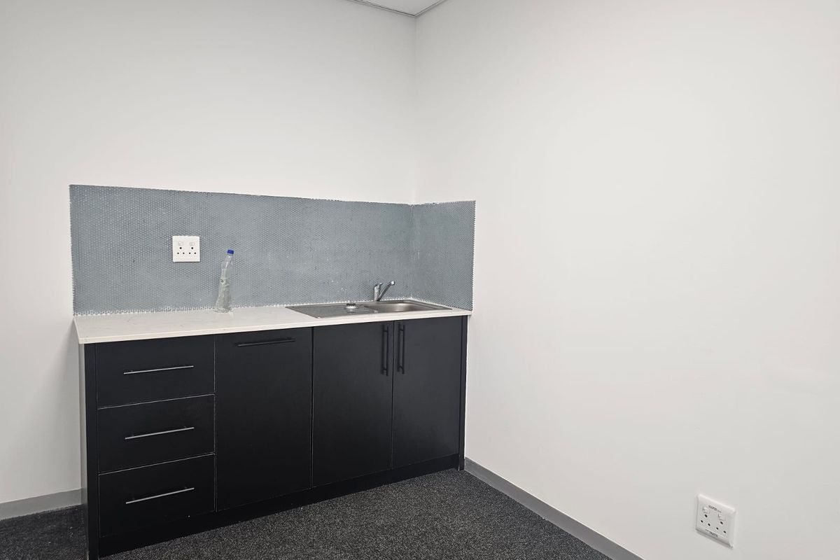 A clean, compact office kitchenette featuring dark cabinetry, a stainless steel sink, and a modern mosaic tile backsplash.