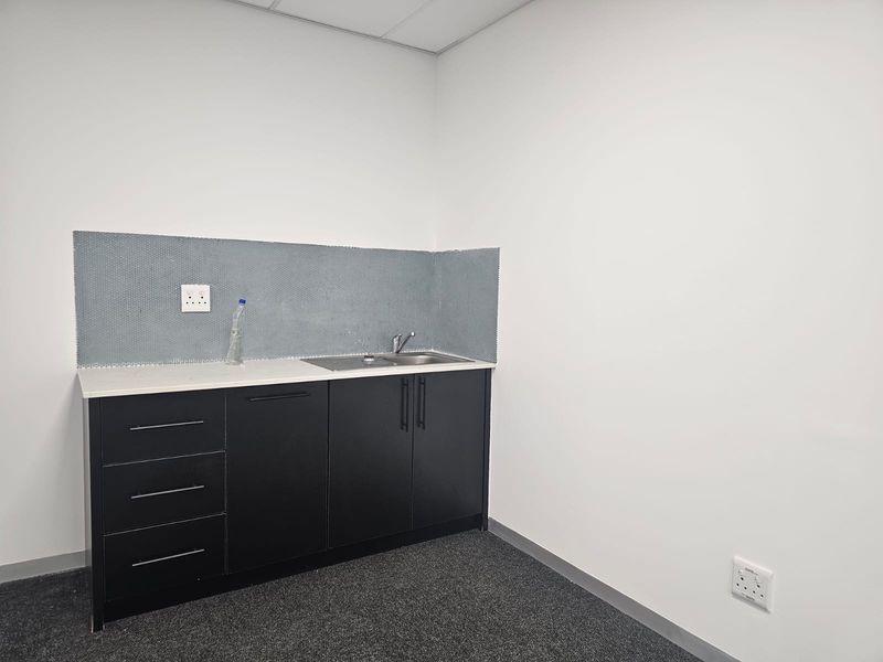 A clean, compact office kitchenette featuring dark cabinetry, a stainless steel sink, and a modern mosaic tile backsplash.