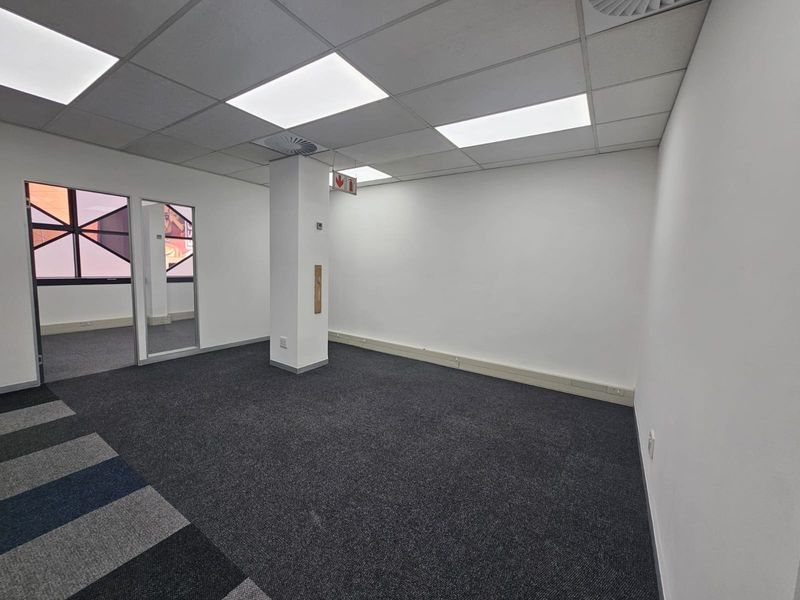 A clean, empty office space featuring carpeted flooring, suspended ceiling with recessed lighting, and integrated air conditioning, suitable for a professional workspace.