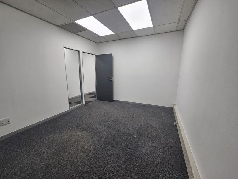 A clean, empty office space featuring carpeted flooring, a suspended ceiling with recessed lighting, and a glass partition door.