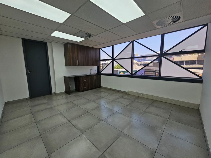A bright, modern office space featuring tiled flooring, a built-in kitchenette unit, and large windows providing ample natural light.