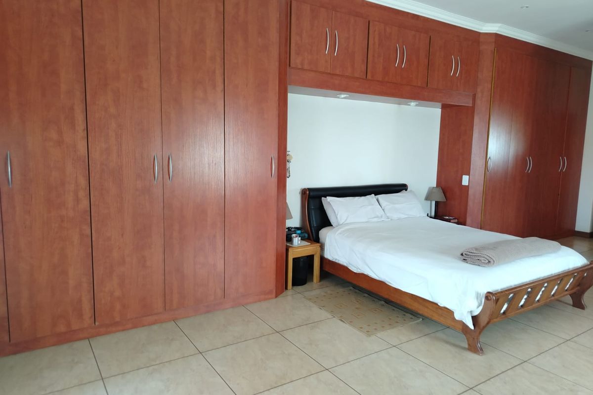 Spacious bedroom featuring extensive built-in wooden cabinetry with overhead storage and neutral tiled flooring.