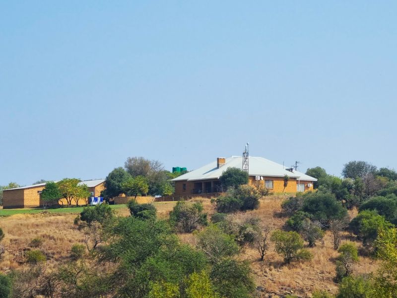 A wide-angle view of a farm property featuring brick buildings with metal roofing, set within a natural landscape with native trees and vegetation.