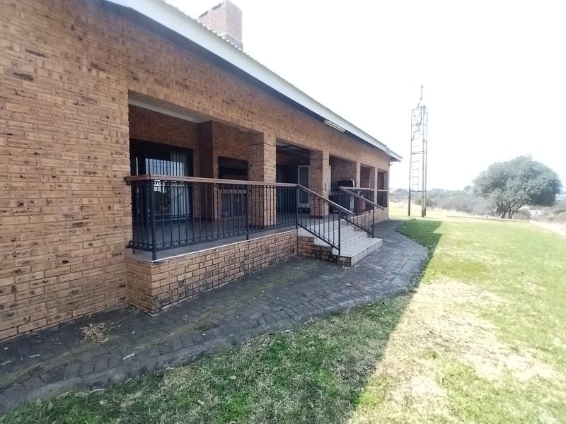 Spacious covered brick patio featuring a built-in braai, wrought iron railings, and direct access to the surrounding garden area.
