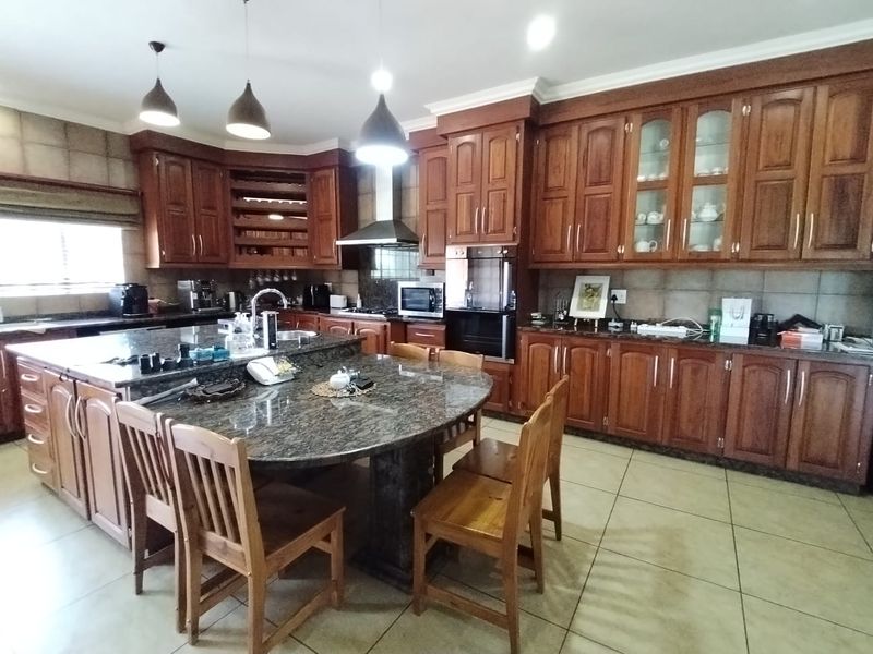 Spacious kitchen featuring extensive wooden cabinetry, granite countertops, a large central island with integrated seating, and built-in appliances.