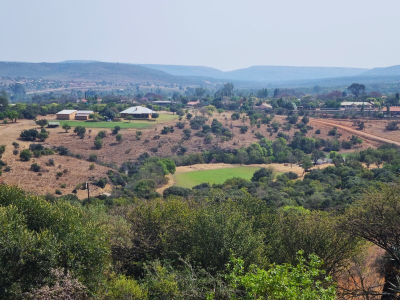 A wide-angle elevated view of the expansive farm landscape, featuring rolling hills, natural vegetation, and distant rural structures.