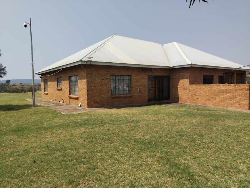 Rear view of a face brick farmhouse featuring a corrugated metal roof, security window bars, and a surrounding lawn area.