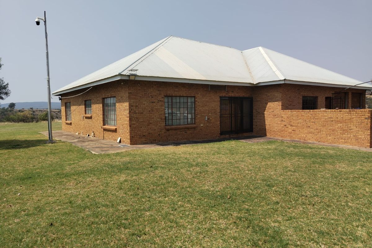 Rear view of a face brick farmhouse featuring a corrugated metal roof, security window bars, and a surrounding lawn area.
