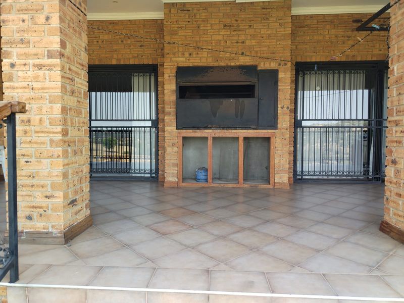 Covered patio area featuring face-brick construction, tiled flooring, and a built-in braai, providing a functional outdoor entertainment space.