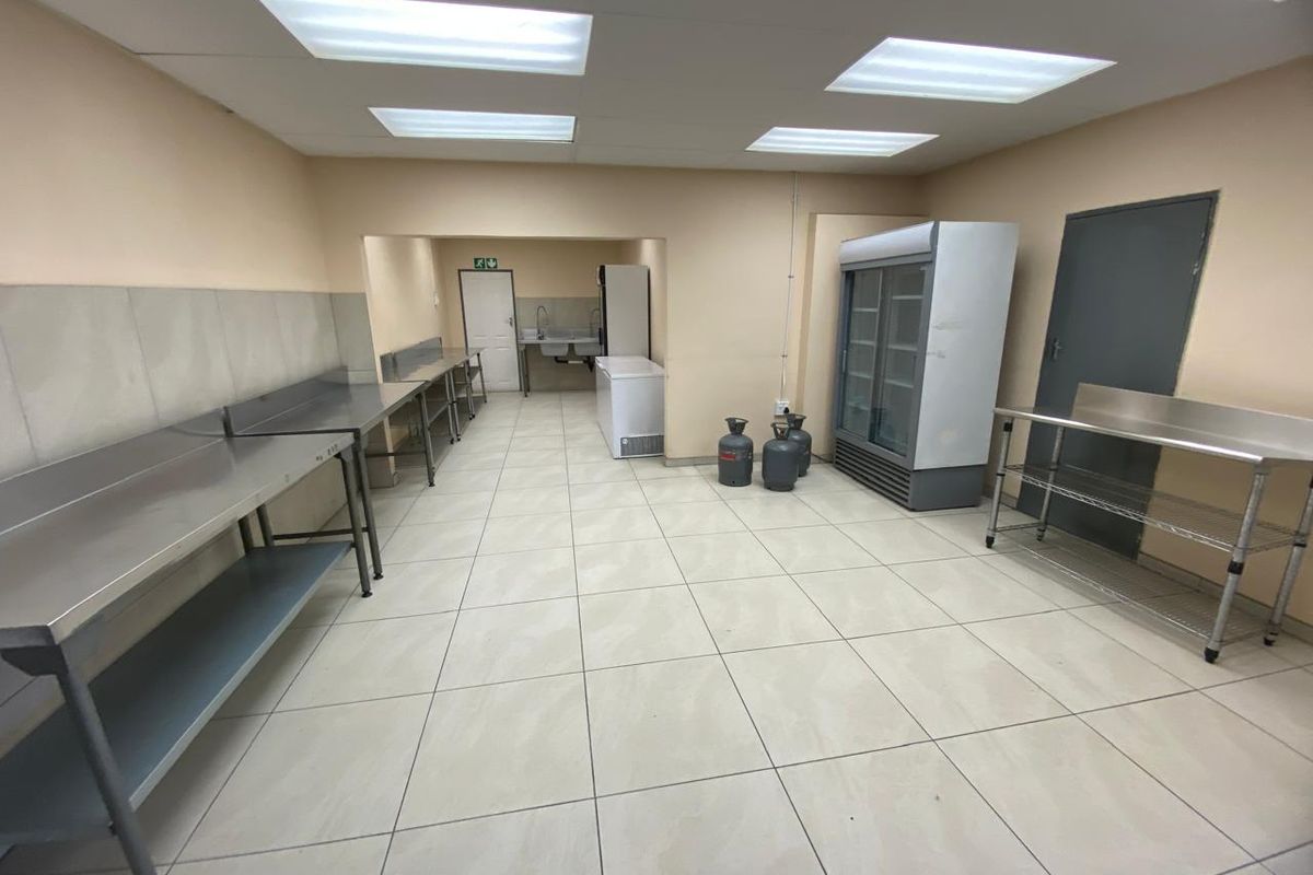 A functional industrial kitchen or food preparation area featuring stainless steel work surfaces, tiled flooring, and recessed ceiling lighting.