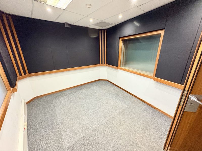 A professional office or recording space featuring acoustic wall paneling, a suspended ceiling with recessed lighting, and an internal viewing window.