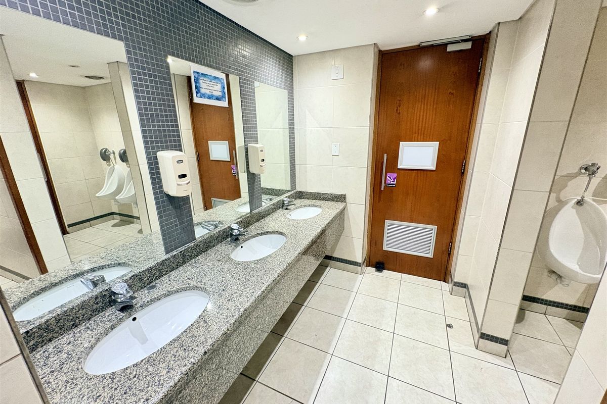 A clean, functional office restroom featuring a granite vanity with dual sinks, mosaic tile accents, and multiple urinals.