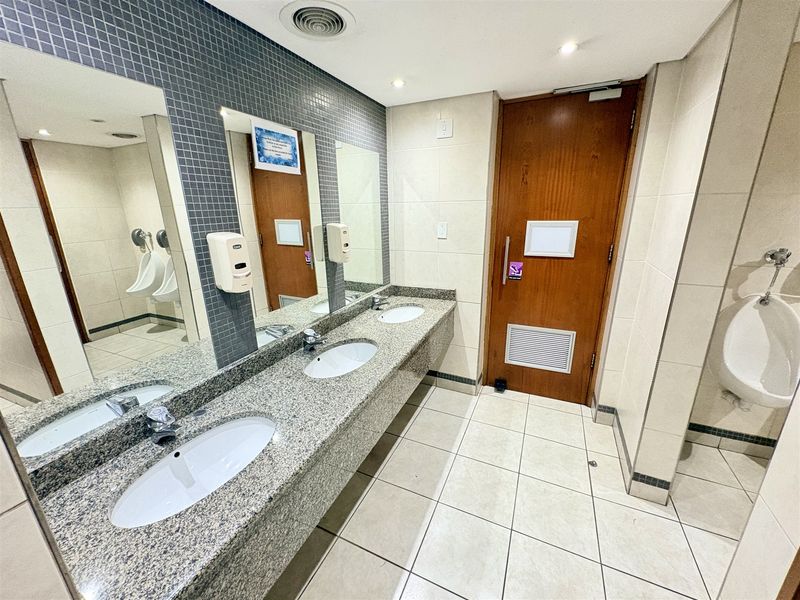 A clean, functional office restroom featuring a granite vanity with dual sinks, mosaic tile accents, and multiple urinals.