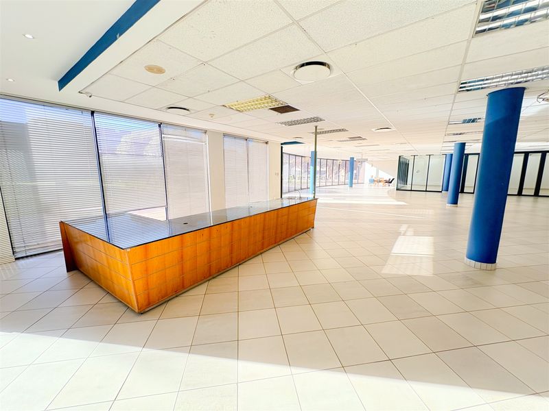 Spacious open-plan office area featuring ceramic tile flooring, a built-in reception desk, large windows with blinds, and modern glass partitioning.