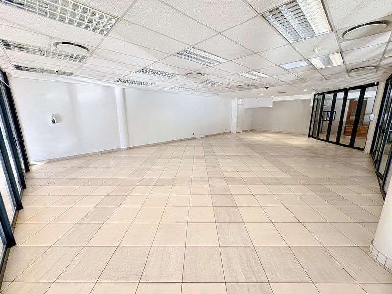 Spacious, open-plan office area featuring neutral ceramic floor tiles, a suspended ceiling with recessed lighting, and modern glass partitioning.