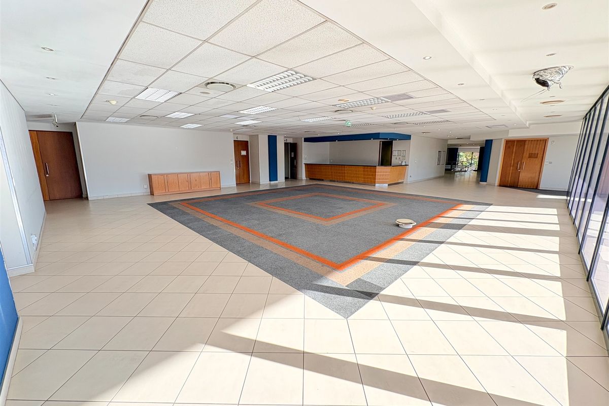 Spacious open-plan office area featuring a reception desk, built-in cabinetry, tiled flooring with carpet inlay, and large windows providing ample natural light.