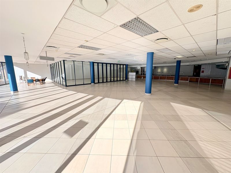Spacious open-plan office area featuring tiled flooring, suspended ceilings, glass-partitioned meeting rooms, and a built-in serving counter.