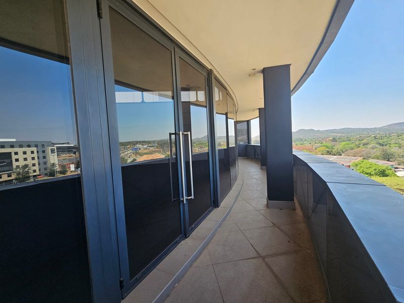 A modern, curved balcony featuring high-quality glass facade panels, tiled flooring, and a sleek metal balustrade with expansive views.