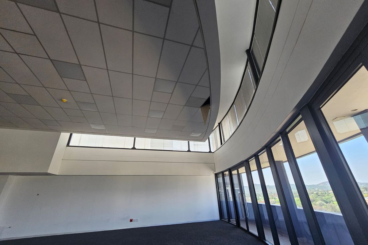 Spacious empty office area featuring a curved suspended ceiling, full-height glass curtain walls, and carpet flooring with expansive exterior views.