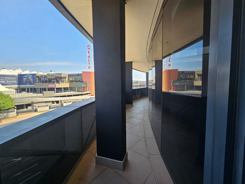A modern, curved balcony featuring tiled flooring, structural columns, and glass balustrades, offering an elevated view of the surrounding commercial area.