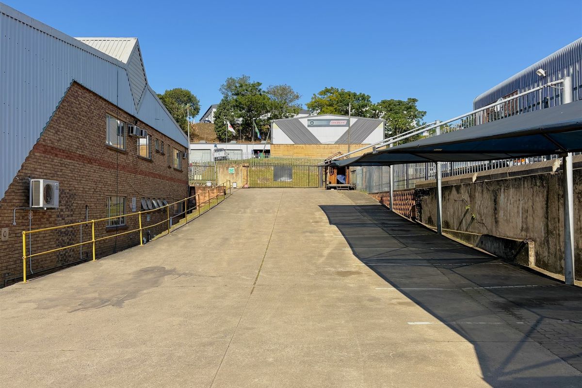 Industrial property exterior featuring a concrete driveway ramp, covered parking bays, and brick building facade with external air conditioning units.