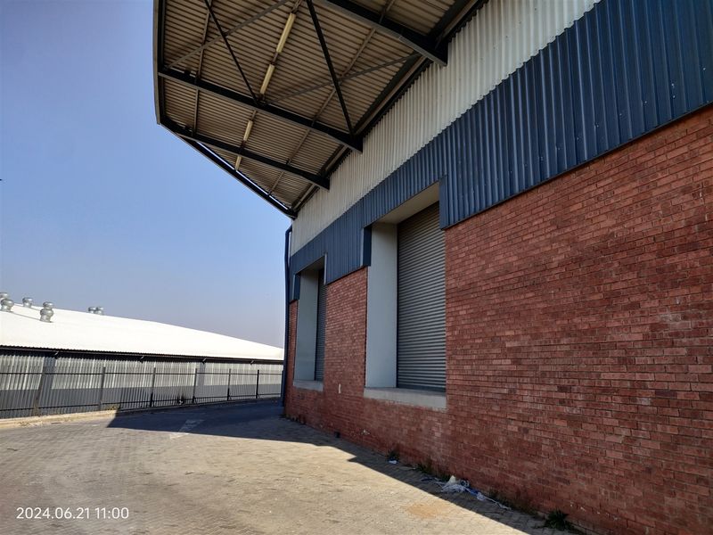 Exterior view of an industrial warehouse featuring a brick facade, corrugated metal cladding, and secure roller shutter doors with a paved yard area.