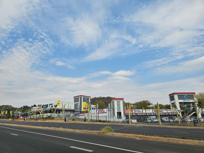A street-level view of the Gift Acres retail complex, showcasing the commercial facade, signage, and surrounding infrastructure from the adjacent road.