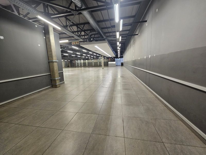 A large, open-plan retail space featuring tiled flooring, exposed industrial ceiling with ductwork, and neutral grey walls, ready for custom fit-out.
