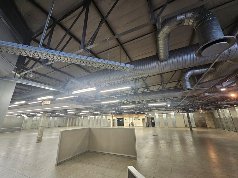 Spacious open-plan retail area featuring high exposed ceilings with industrial ductwork, tiled flooring, and ample lighting, suitable for various commercial uses.