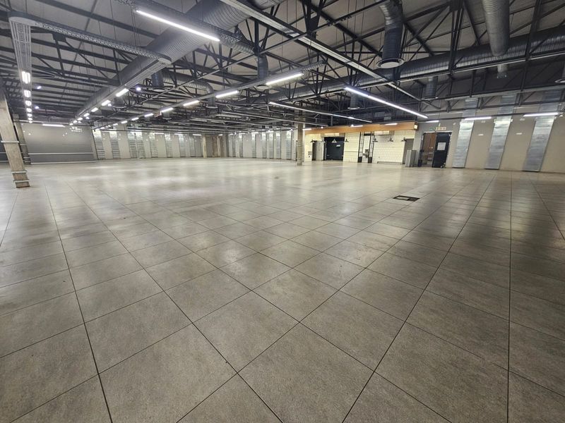 Expansive open-plan retail space featuring high exposed industrial ceilings, polished tiled flooring, and modern linear lighting, suitable for various commercial applications.
