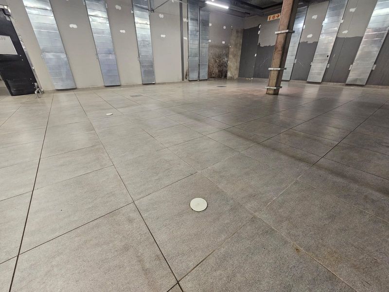 A spacious, empty retail unit featuring tiled flooring, exposed HVAC ducting, and a central structural timber column, ready for custom fit-out.
