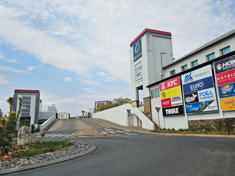 Front view of a retail shopping center featuring a concrete access ramp, paved driveway, and prominent tenant signage on the building facade.