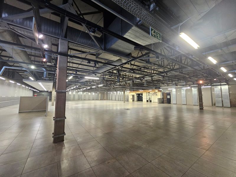 Expansive open-plan retail space featuring high exposed ceilings, industrial ductwork, tiled flooring, and structural steel columns, suitable for various commercial applications.