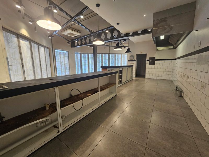 A spacious commercial kitchen area featuring industrial-style exposed beams, tiled walls, a large service counter, and professional extractor hood.