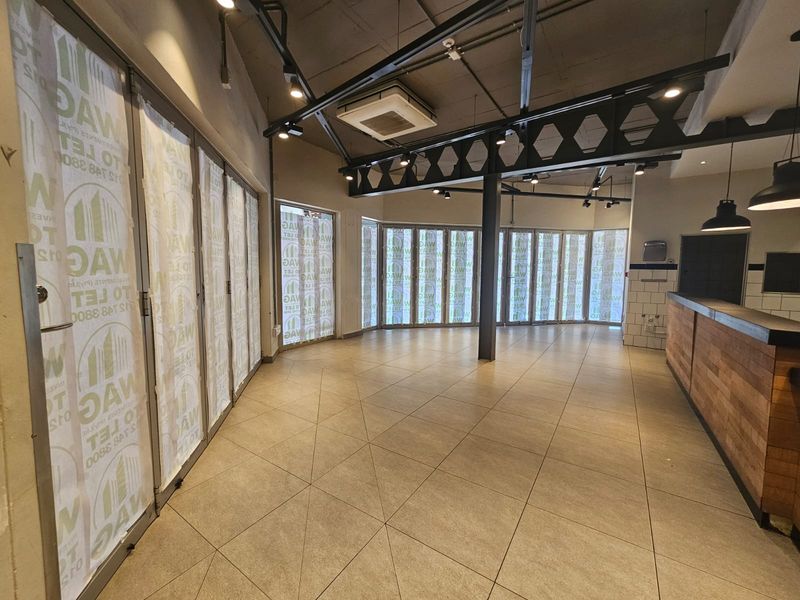 Spacious open-plan retail area featuring tiled floors, exposed industrial ceiling, track lighting, and a built-in service counter with large folding glass doors.