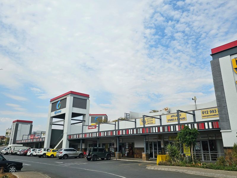 Front elevation of a retail shopping center featuring multiple storefronts, a covered walkway, and an adjacent paved parking area.