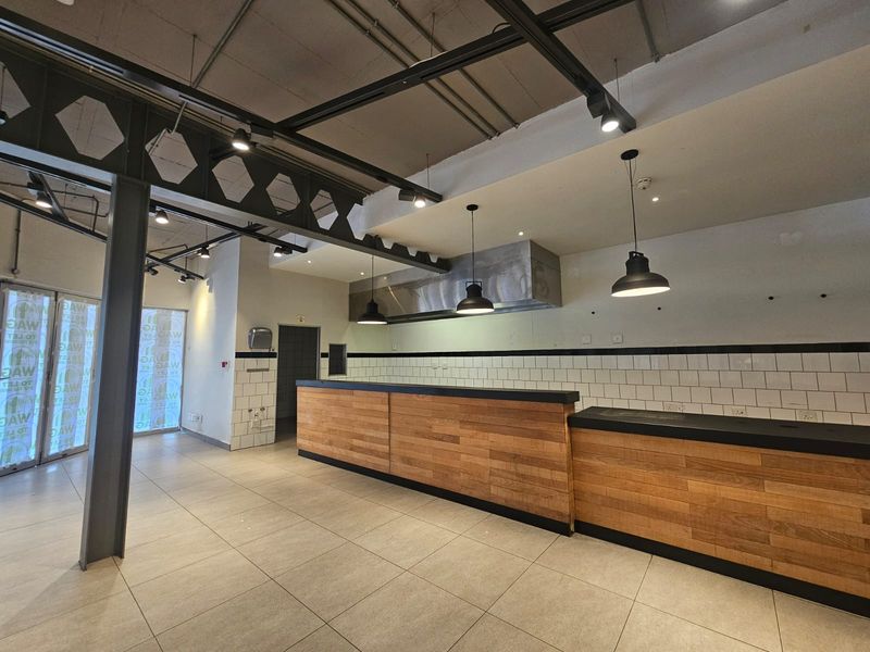 A modern commercial kitchen space featuring an industrial aesthetic with exposed ceilings, a timber-clad service counter, and professional stainless steel extractor hood.