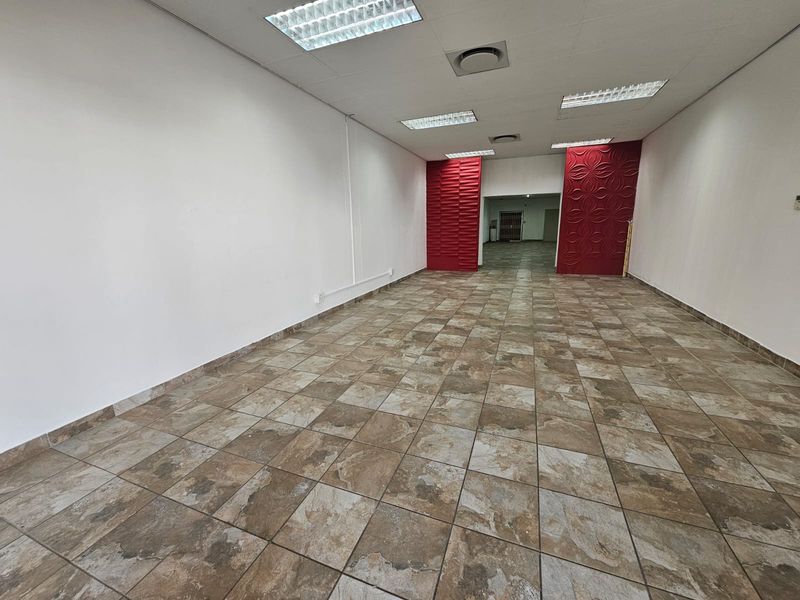 An empty, open-plan retail space featuring tiled flooring, recessed lighting, air conditioning vents, and decorative red feature wall panels.