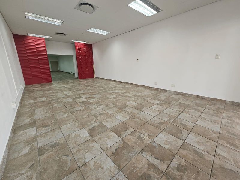 An empty open-plan retail space featuring ceramic tiled flooring, recessed lighting, and distinctive red decorative wall panels.
