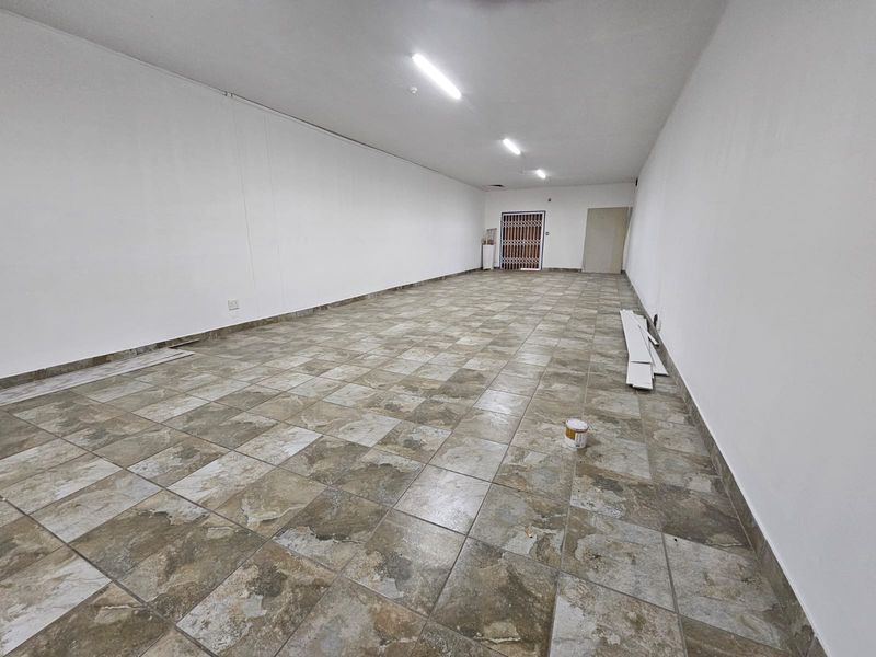A spacious, empty retail unit featuring neutral white walls, durable ceramic tile flooring, and overhead fluorescent lighting, ready for custom fit-out.