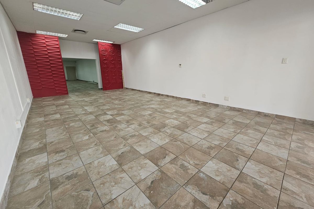 An empty open-plan retail space featuring ceramic tiled flooring, recessed lighting, and distinctive red decorative wall panels.