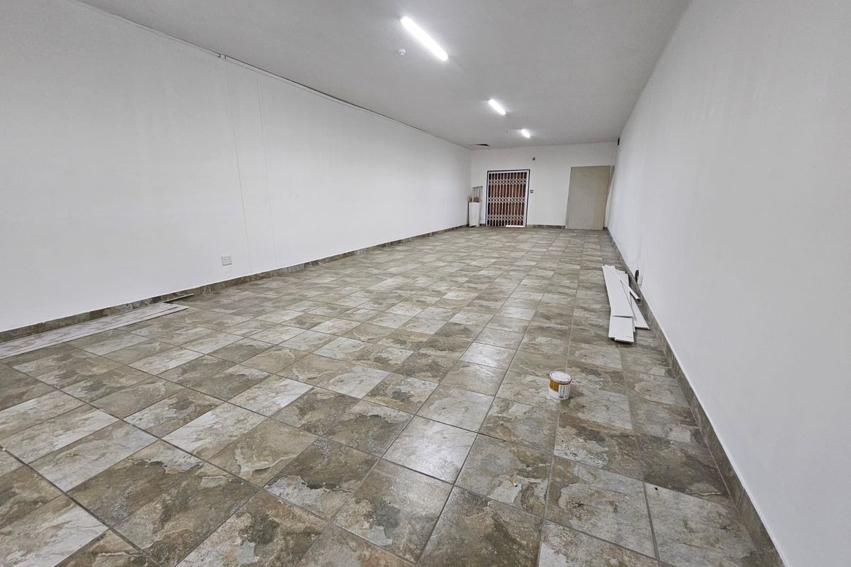 A spacious, empty retail unit featuring neutral white walls, durable ceramic tile flooring, and overhead fluorescent lighting, ready for custom fit-out.