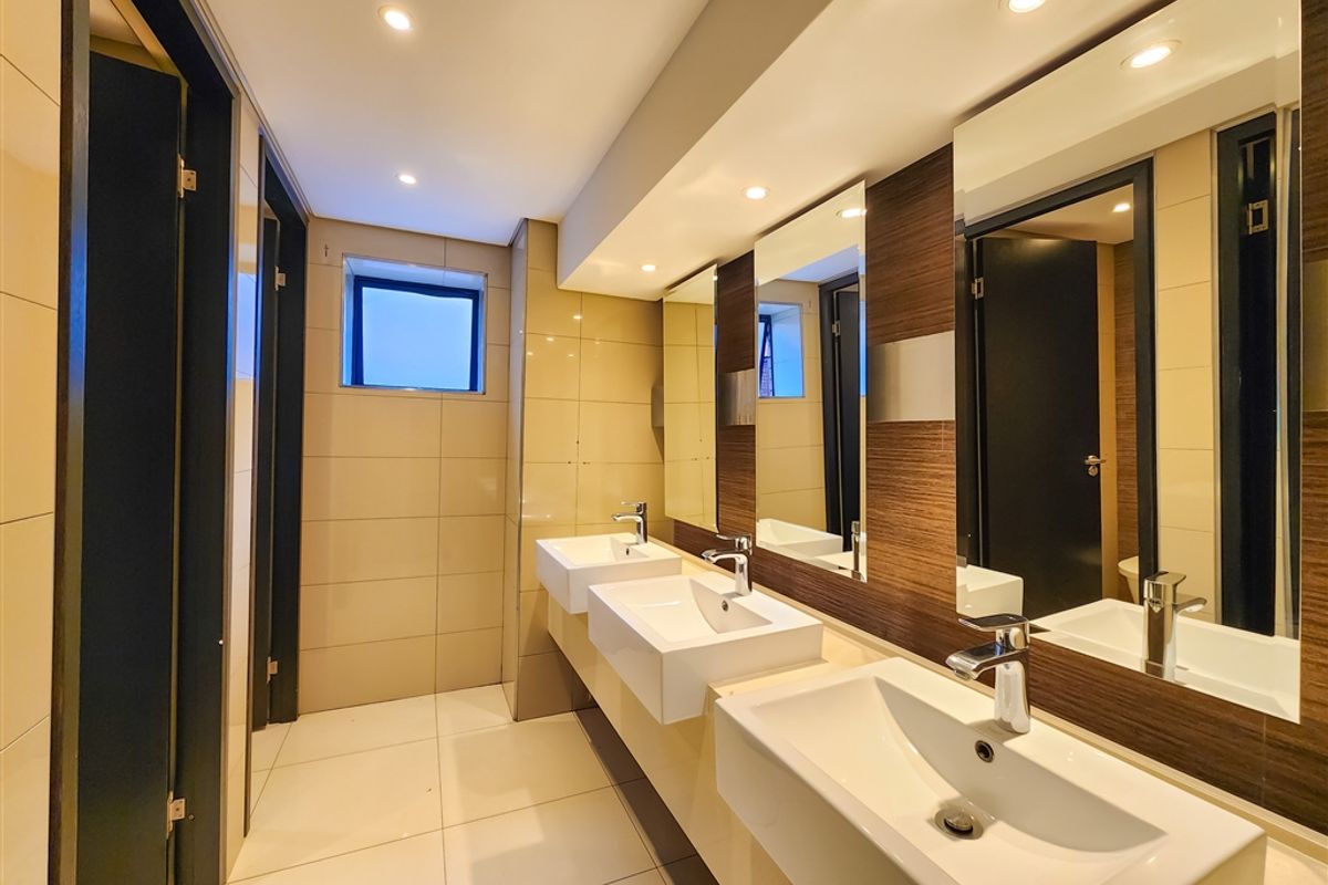 Modern office bathroom featuring a triple vanity with ceramic basins, chrome fixtures, recessed lighting, and contemporary wall and floor tiling.