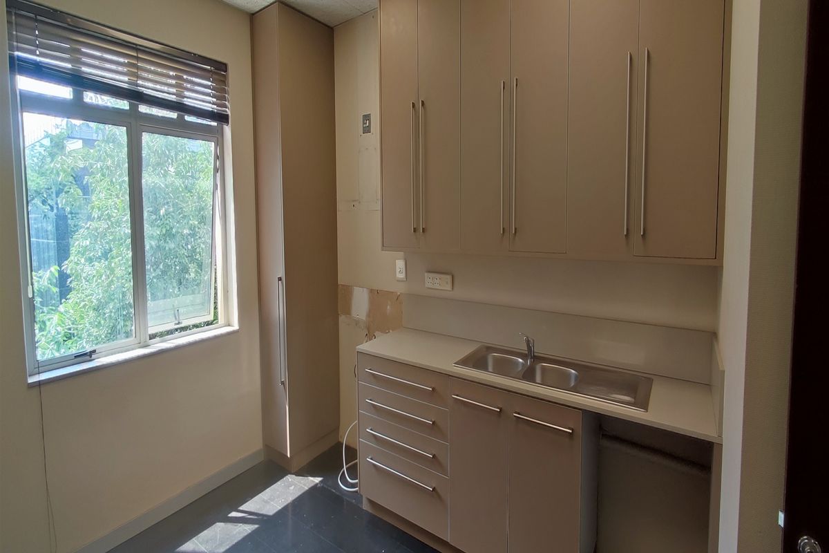 A small office kitchenette featuring built-in cabinetry, a stainless steel sink, and a window providing natural light.